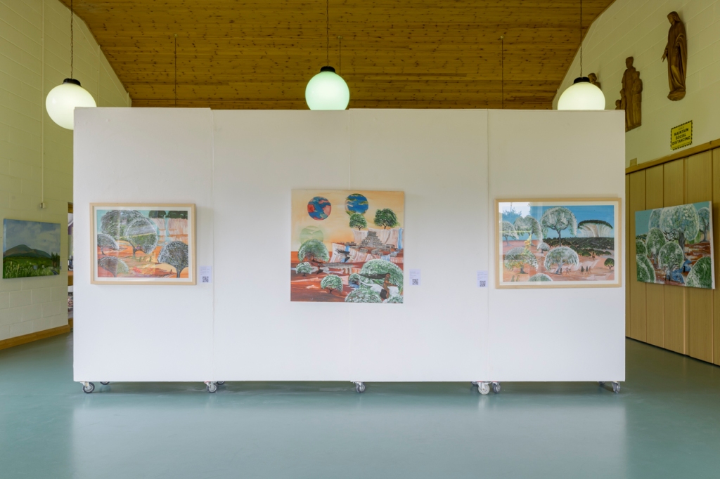 Installation shot of exhibition. In the centre three paintings hang on a white wall in a high ceilinged room. There are other paintings hanging on the wall in the background.